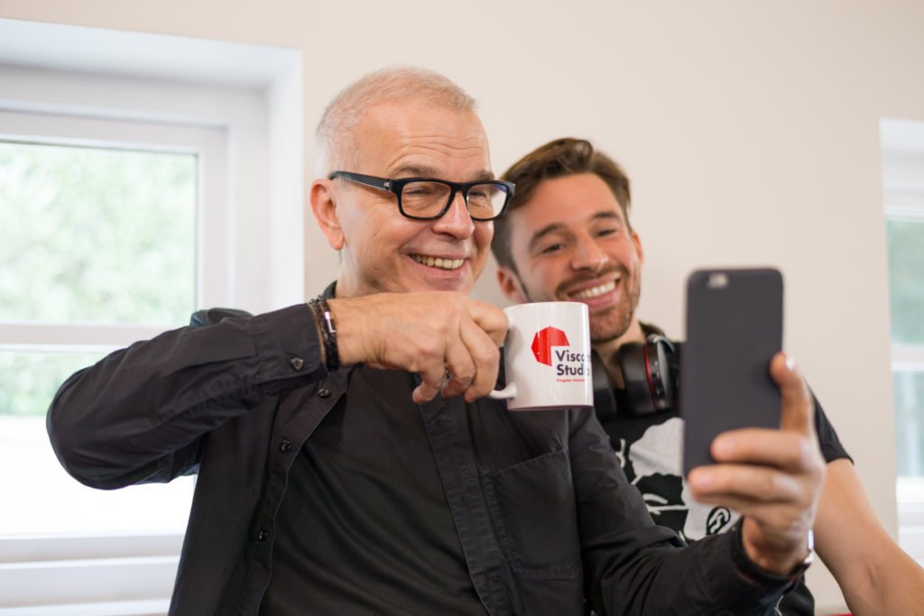 Tony Visconti taking a selfie with a musician, holding the Visconti Studio-branded mug
