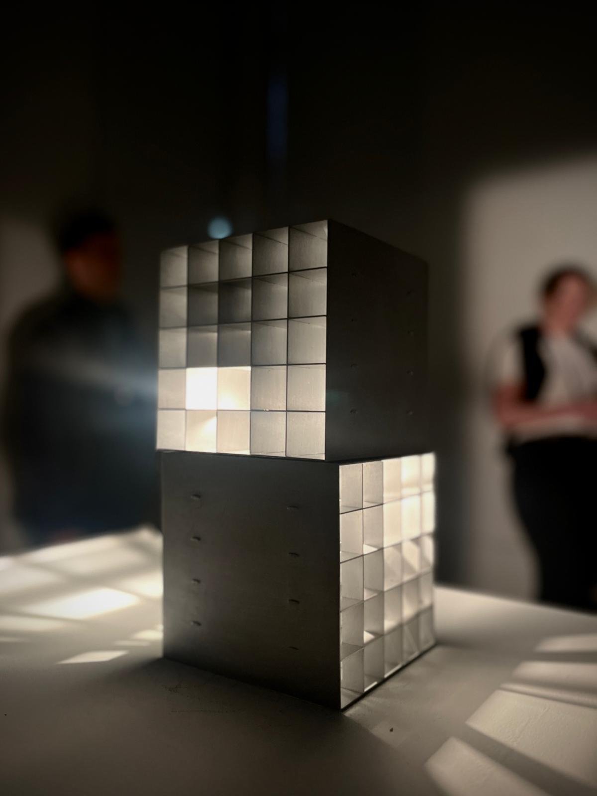 The kinetic Circadia light sculpture, shown on a white table, in a darkened room with out of focus figures in the background