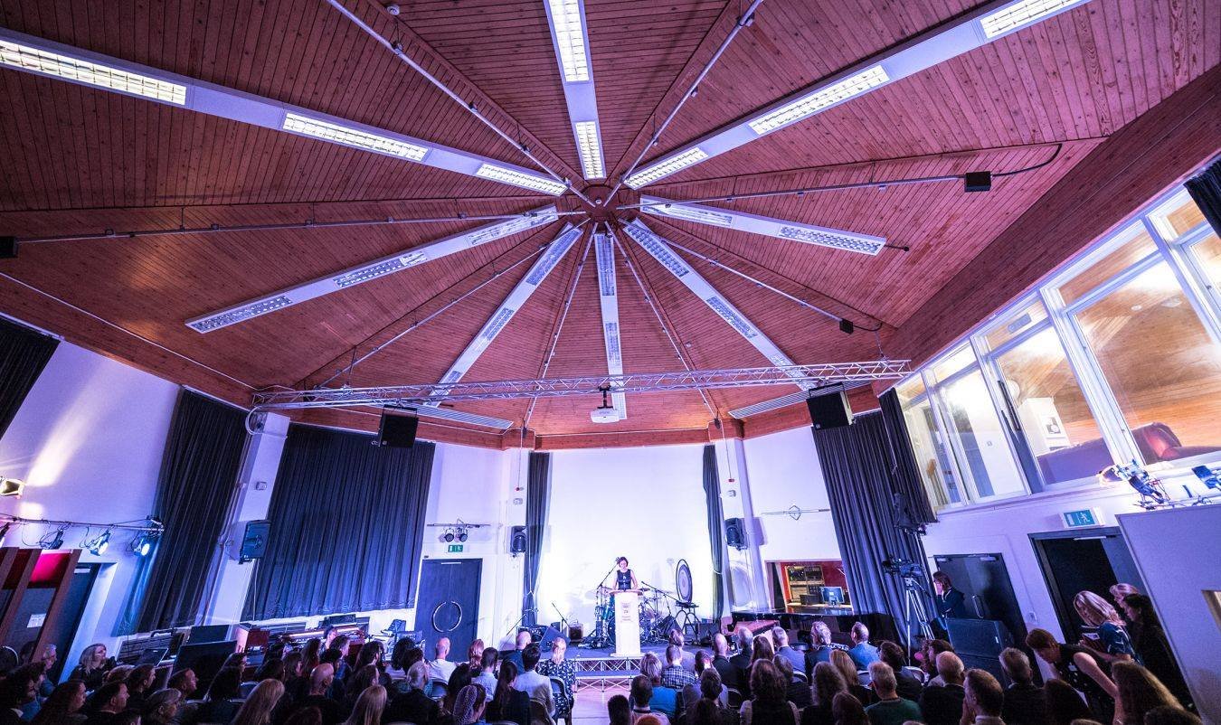 An audience filling the live room for an event, with the octagonal timber ceiling and lighting rig overhead