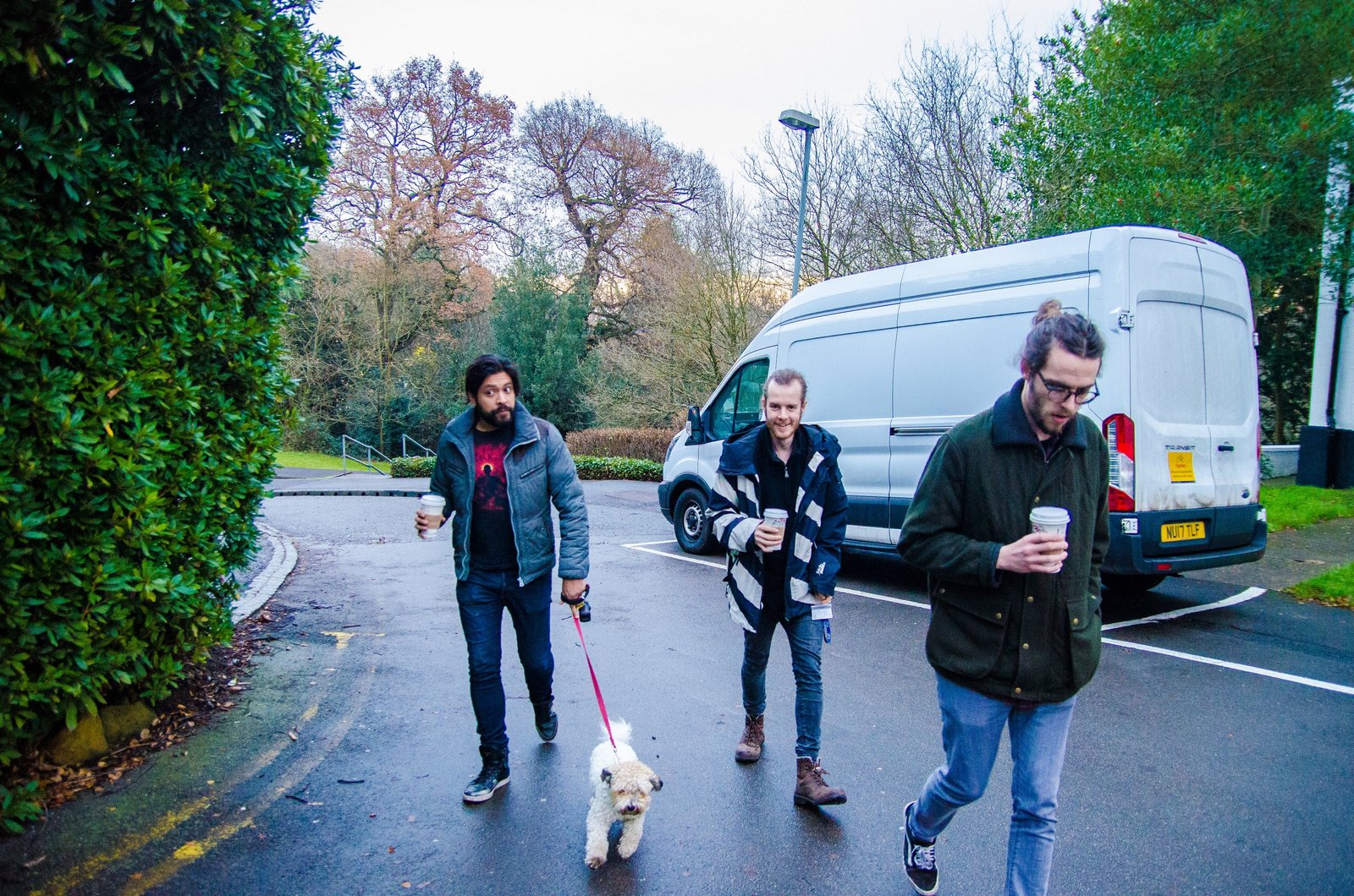 Three musicians with coffee cups walking up the driveway towards the studio