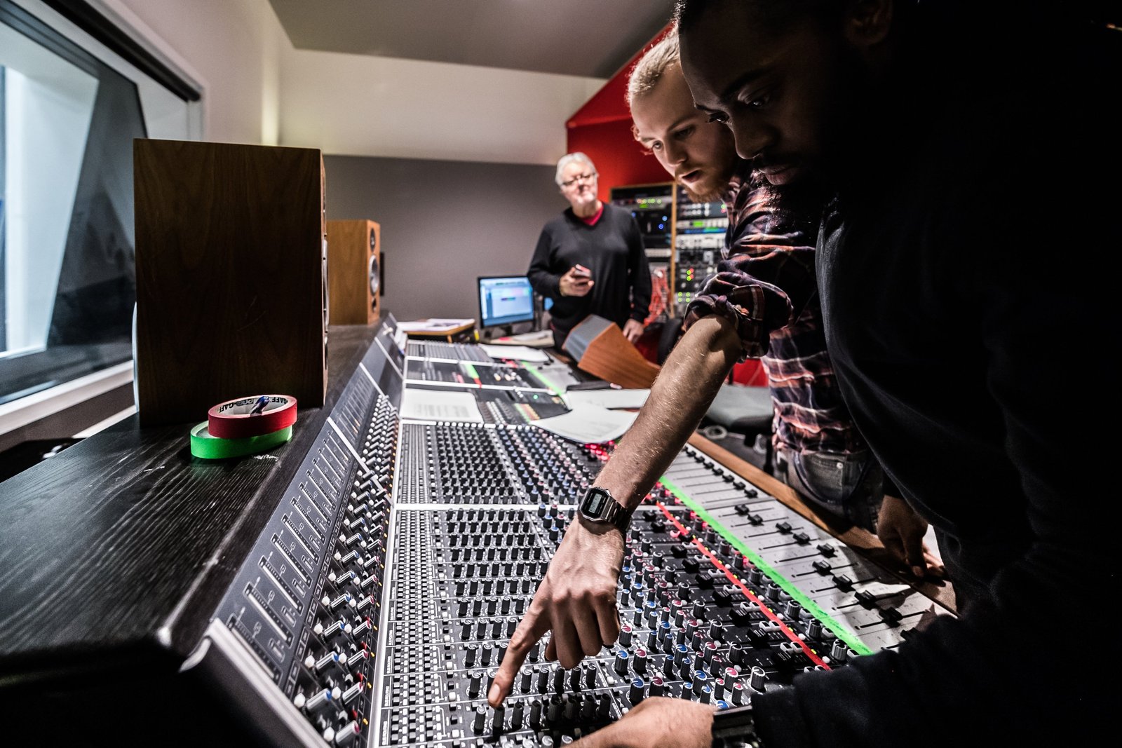 Two students at the Audient console during a Winterschool session, one pointing out a channel strip to the other, with Chris Kimsey watching from behind the desk