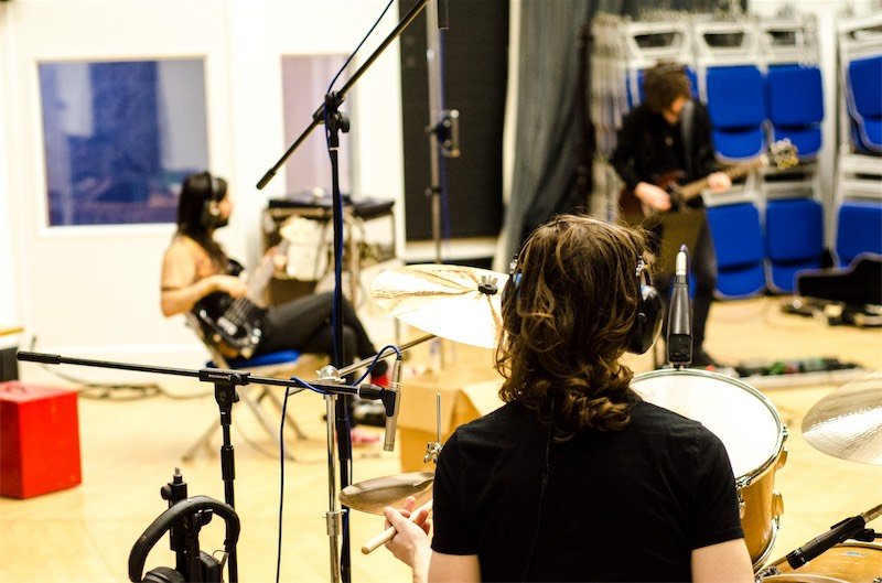 A band tracking live, seen from behind the drum kit