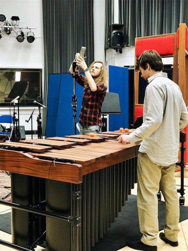 Studio engineer setting up a microphone near a marimba in the live room