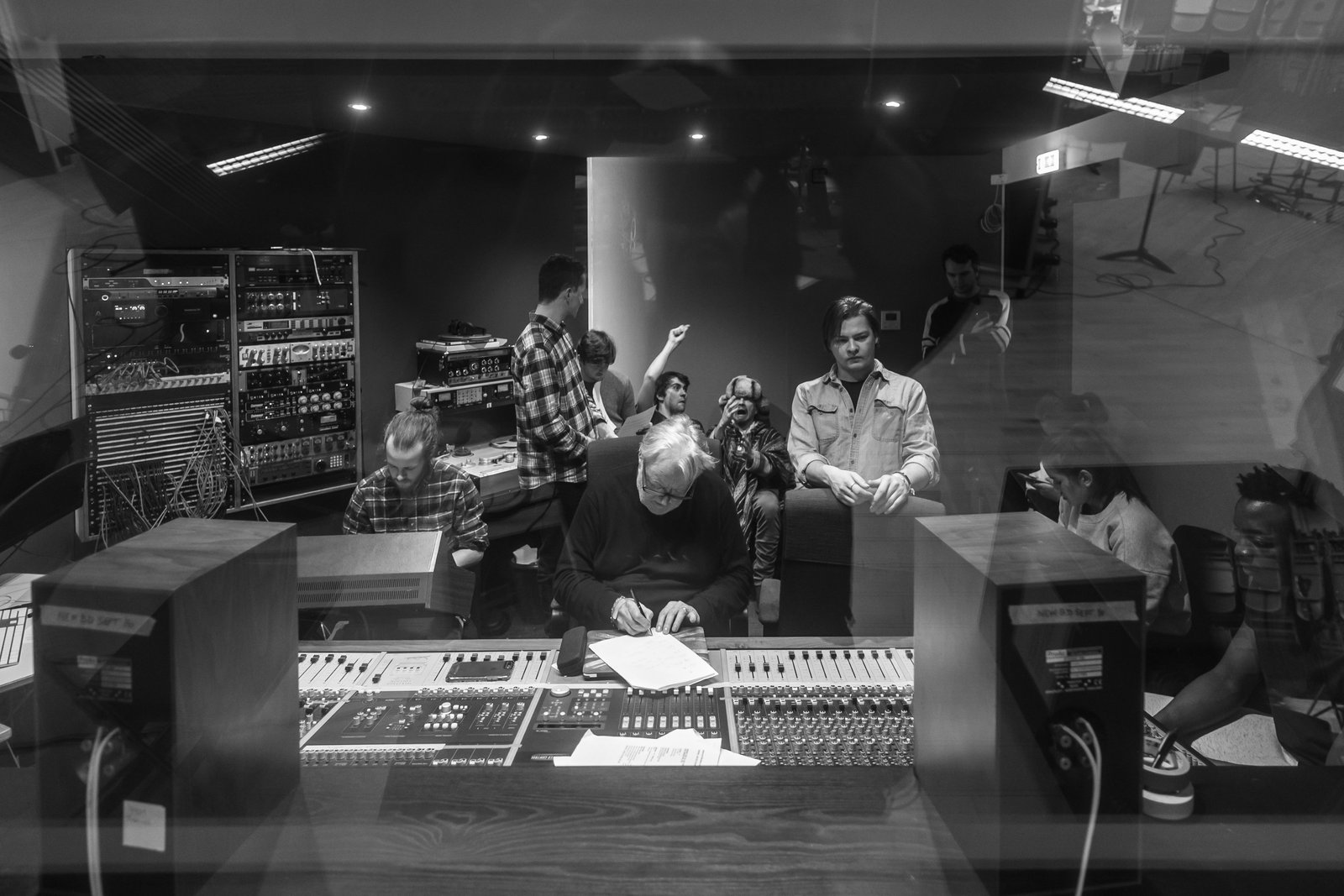 A session in progress in the control room, seen through the glass from above, with a producer writing at the desk and students gathered behind